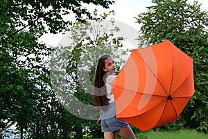 beautiful young girl in white T-shirt holds an orange umbrella, Walking on sunny summer day outdoors against background of green