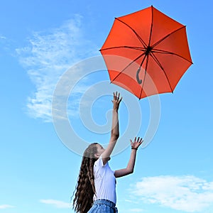 beautiful young girl white T-shirt throws up an orange umbrella. A flying umbrella against blue summer sky.