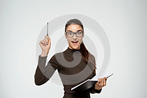 Beautiful young girl writing in notebook and got an idea. Looking at camera. Over white background