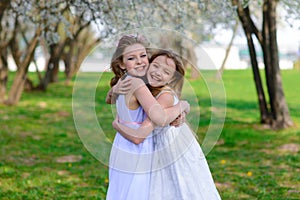 Young girls with blue eyes in white dresses in garden with apple trees blosoming