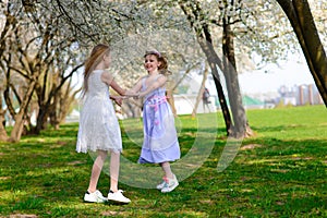 Young girls with blue eyes in white dresses in garden with apple trees blosoming