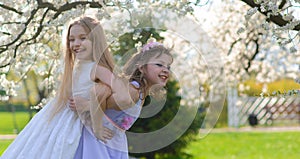 Young girls with blue eyes in white dresses in garden with apple trees blosoming