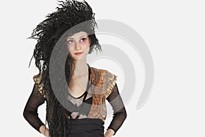 Beautiful young Goth woman with teased hair looking away over gray background