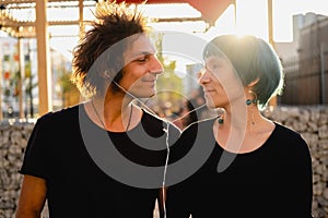 Beautiful young guy and girl listen to music together from mobile phone. Couple in love are sitting face to face at sunset