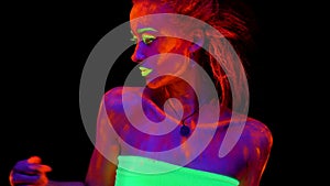 A beautiful young half-naked girl dancing with glowing paint on her body in black light. Pretty woman with glowing