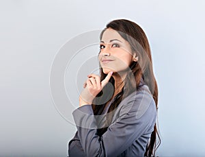 Beautiful young happy business woman with finger under the face thinking and looking up in grey suit and long hair. Closeup