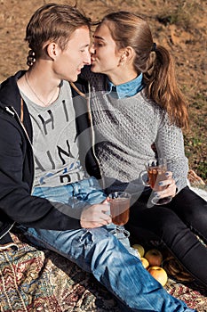 Beautiful young happy couple in love sitting on lake shore on a warm Sunny evening kissing and drinking warm tea