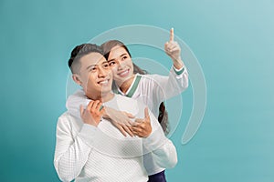 Beautiful young happy couple love smiling embracing point finger to empty copy space, man and woman smile looking up