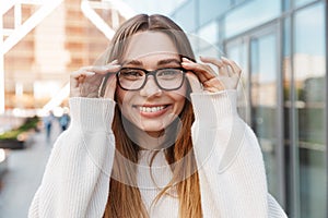 Beautiful young happy excited business woman posing walking outdoors near business center wearing eyeglasses