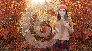 Beautiful young happy girl with a bright red-yellow autumn leaf and cup of coffee in the park