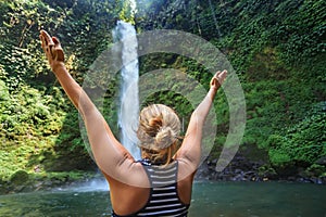 Beautiful young happy girl enjoying nature under tropical fresh waterfall