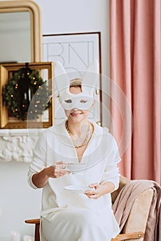 Beautiful young happy woman in carnival rabbit mask and white costume celebrating a new one in a modern christmas interior.