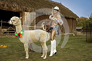 Beautiful young happy woman with cute alpacas on a summer day at the alpaca ranch. Pretty Girl with alpacas