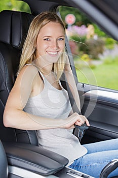 Beautiful young happy woman fastens seat belt in car