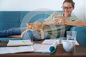 Beautiful young happy woman in glasses uses a smartphone on the couch, a cute red cat lap