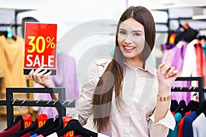 Beautiful young happy woman holiding red sale sign in a clothing