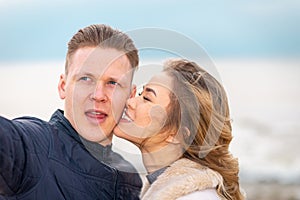 Beautiful young happy woman hugging cuddle young boyfriend while taking selfie photo on sunny beach.Close up