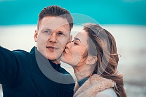 Beautiful young happy woman kissing and hugging boyfriend while taking selfie photo on sunny beach.Close up