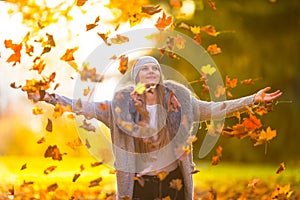 Beautiful young happy woman playing with autumn leaves.