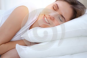 Beautiful young and happy woman sleeping while lying in bed comfortably and blissfully smiling