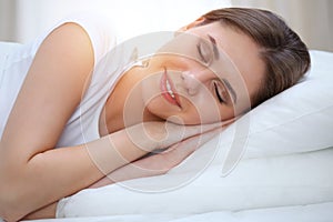 Beautiful young and happy woman sleeping while lying in bed comfortably and blissfully smiling