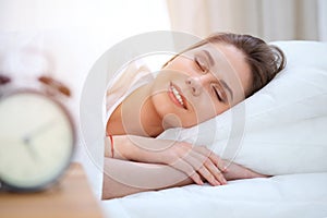 Beautiful young and happy woman sleeping while lying in bed comfortably and blissfully smiling