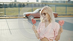 Beautiful young happy woman on the street with two colored lollipop at sunset