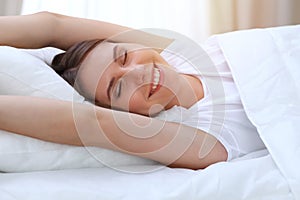 Beautiful young and happy woman stretching hands while lying in bed comfortably and blissfully smiling befor wake up in