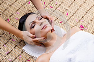 Beautiful, young and healthy woman on bamboo mat in spa salon having face massage.