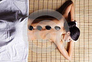Beautiful, young and healthy woman on bamboo mat in spa salon is having hot stone massage.