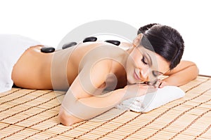 Beautiful, young and healthy woman on bamboo mat in spa salon is having hot stone massage.