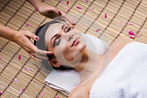 Beautiful, young and healthy woman on bamboo mat in spa salon having temple massage.