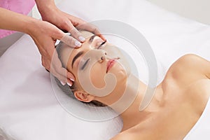 Beautiful, young and healthy woman having face massage in spa salon. Hands of professinal masseur. Spa, health and