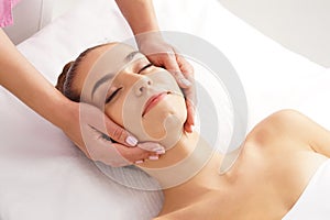 Beautiful, young and healthy woman having face massage in spa salon. Hands of professinal masseur. Spa, health and