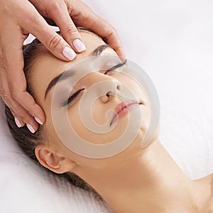Beautiful, young and healthy woman having face massage in spa salon. Hands of professinal masseur. Spa, health and