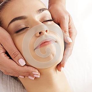 Beautiful, young and healthy woman having face massage in spa salon. Hands of professinal masseur. Spa, health and