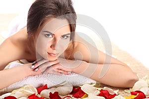 Beautiful, young and healthy woman in spa on mat with rose petals. Spa, health and healing concept.