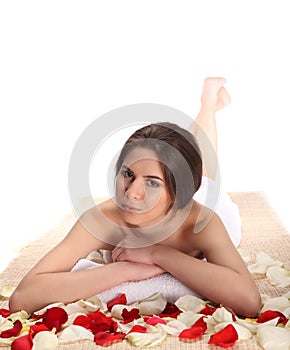 Beautiful, young and healthy woman in spa salon on bamboo mat with rose petals. Spa, health and healing concept.