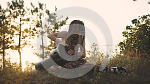 Beautiful young hippie woman with dreadlocks playing on djembe. Funky woman drumming in nature on an ethnic drum at sunset or sunr