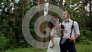 Beautiful young hipster couple curly bride posing in forest. The groom holds in his hands a magnificent bouquet.