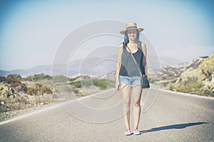 beautiful young hipster girl in hat standing on the road, against the backdrop of beautiful mountain landscape