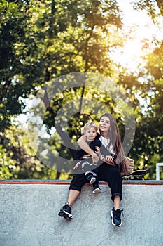 Beautiful young hipster mom and little son at the skatepark