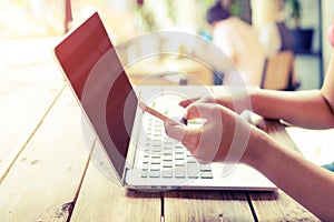 Beautiful young hipster woman`s hands busy working on her laptop, female using cell telephone sitting at wooden table in a coffee