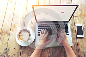 Beautiful young hipster woman`s hands busy working on her laptop sitting at wooden table in a coffee shop