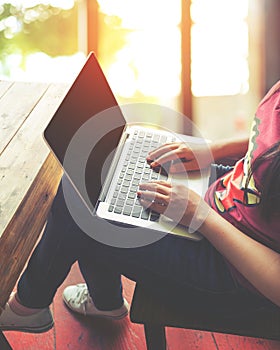 Beautiful young hipster woman`s hands busy working on her laptop sitting at wooden table in a coffee shop
