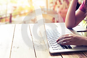 beautiful young hipster woman`s hands busy working on her laptop sitting at wooden table in a coffee shop