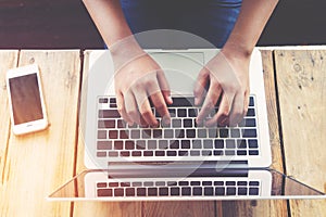 Beautiful young hipster woman`s hands busy working on her laptop sitting at wooden table in a coffee shop