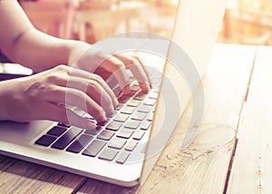 beautiful young hipster woman`s hands busy working on her laptop sitting at wooden table in a coffee shop