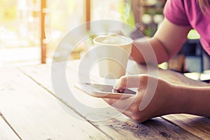 beautiful young hipster woman`s hands holding mobile smart phone with hot coffee cup at cafe shop