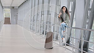Beautiful young hispanic woman traveler happy girl female student tourist with suitcase sitting in airport terminal near